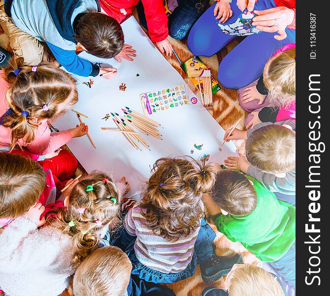 Several small children draw on a sheet of paper with pencils. A view from above.