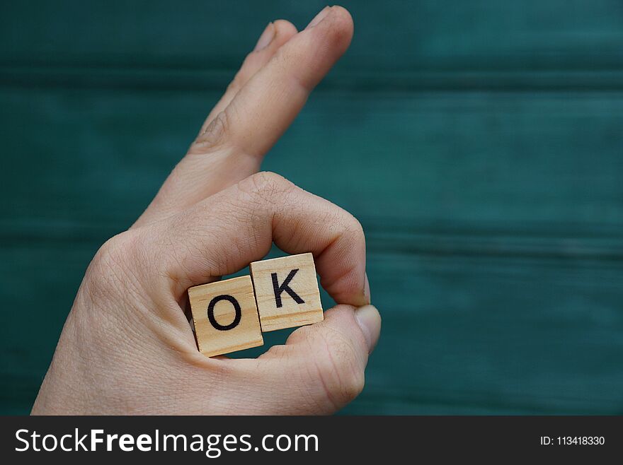 Hand gesture and wooden letters with the word ok on a green background