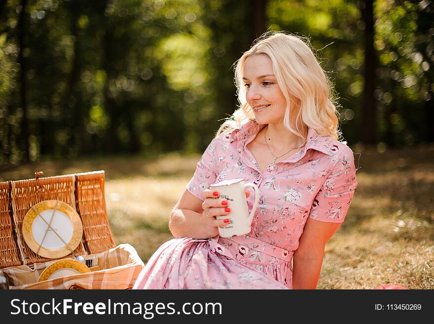 Beautiful and young blonde woman sitting and holding a cup on picnic in the forest. Beautiful and young blonde woman sitting and holding a cup on picnic in the forest