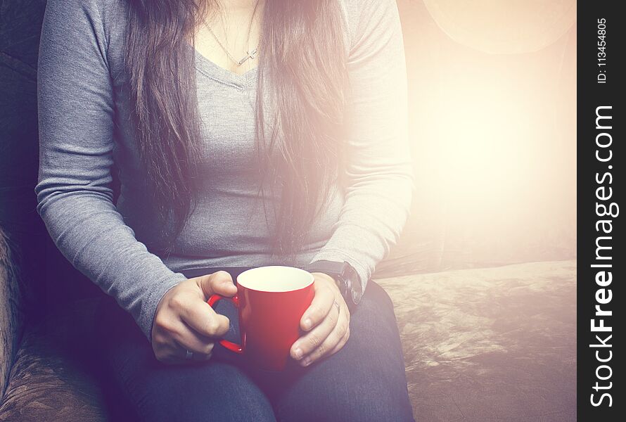 The girl is sitting on the couch and drinking a hot drink ..