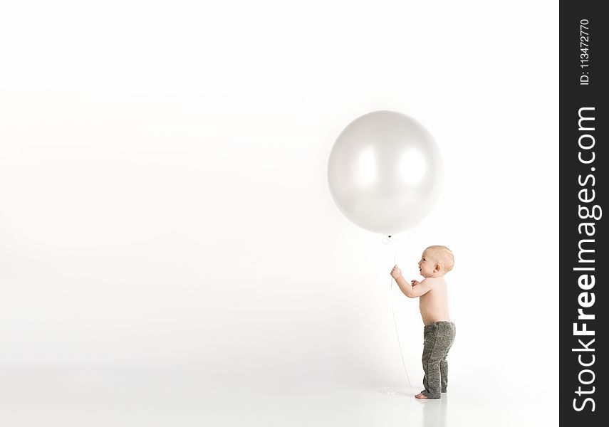 Baby in Black Pants Holding White Balloon While Standing