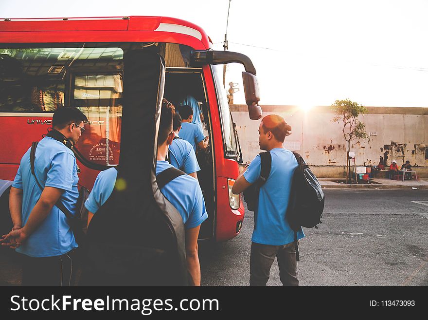 Group of Men Wearing Blue Shirts About to Enter Red Bus
