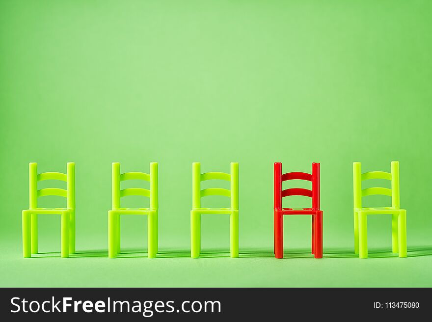 Unique red chair in row of green others. Leadership concept. Empty chairs by wall. The concept of uniqueness, distinction from others.