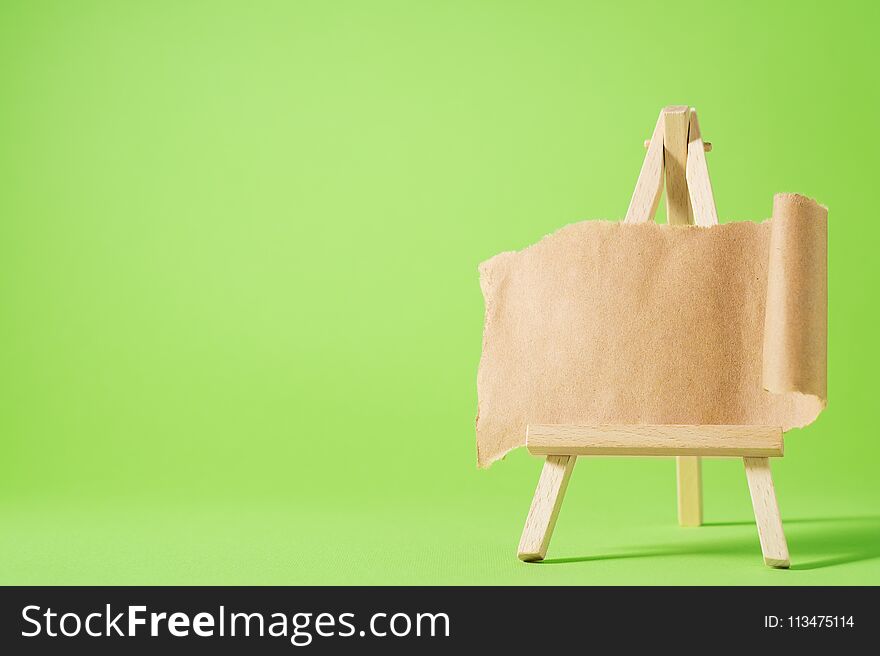 Small easel with blank paper on green background. Torn sheet of paper on easel. Place for your text.