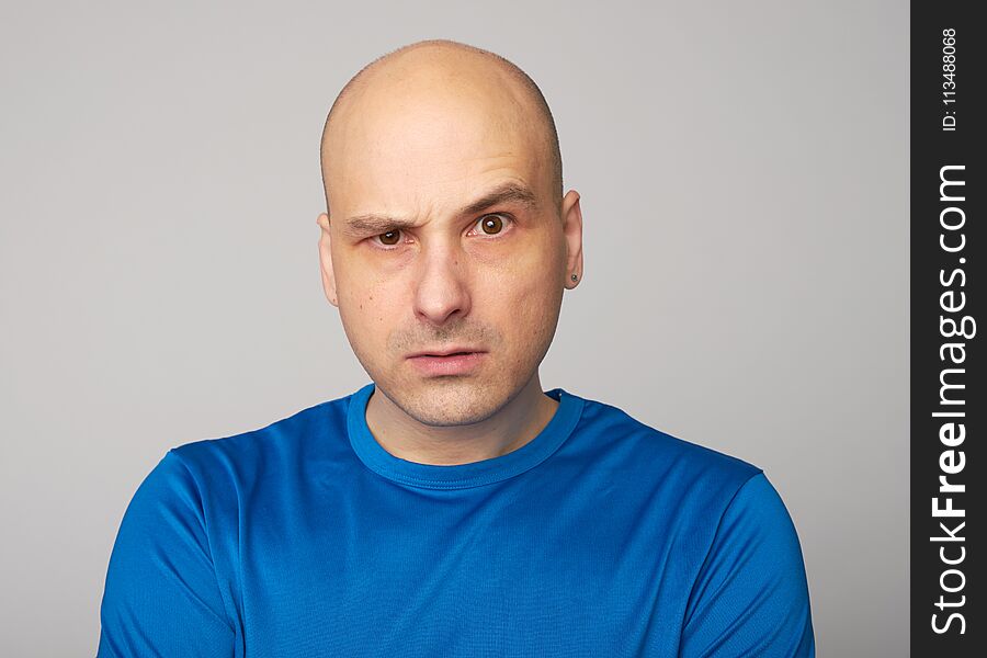 Serious bald man with raised eyebrow looking at camera. Displeased guy isolated over grey background