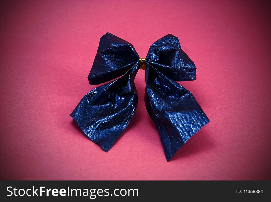 A macro picture of a shiny blue paper bow against a pink background