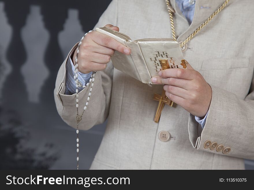 Detail of the hands of a communion child dressed in a beige suit and holding a book and a rosary