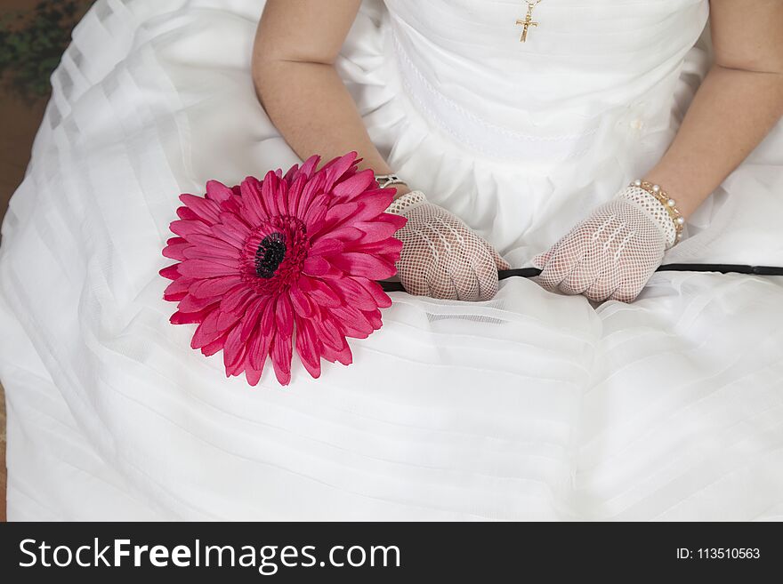 Detail of the hands of a communion girl dressed in white with a flower in her hands