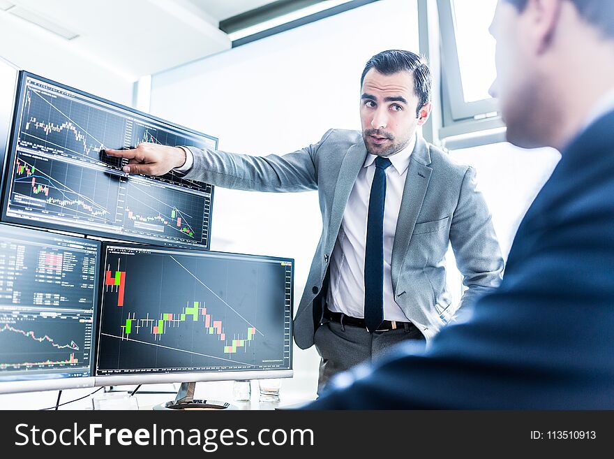 Businessmen trading stocks online. Stock brokers looking at graphs, indexes and numbers on multiple computer screens. Colleagues in discussion in traders office. Business success concept. Businessmen trading stocks online. Stock brokers looking at graphs, indexes and numbers on multiple computer screens. Colleagues in discussion in traders office. Business success concept.