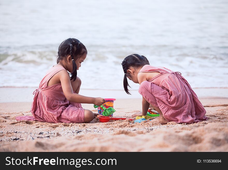 Two cute asian little child girls having fun to play with sand on beach together in summer vacation
