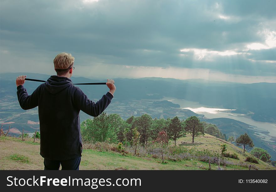 Man Wearing Hoodie Standing on Mountain Under Cloudy Sky