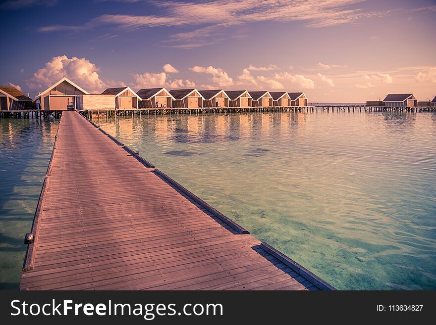 Sunset on Maldives island, luxury water villas resort and wooden pier. Beautiful sky and clouds and beach background for summer vacation holiday and travel concept. Sunset on Maldives island, luxury water villas resort and wooden pier. Beautiful sky and clouds and beach background for summer vacation holiday and travel concept