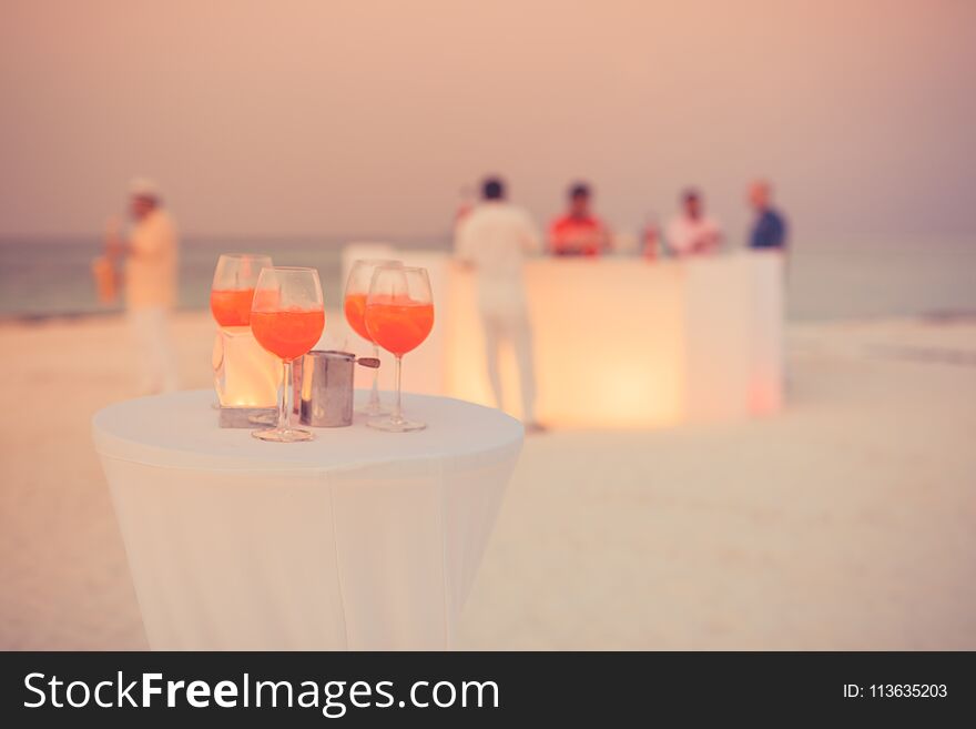 Aperol cocktail glasses on simple white table. Beach party background with drinks and blurred people in background