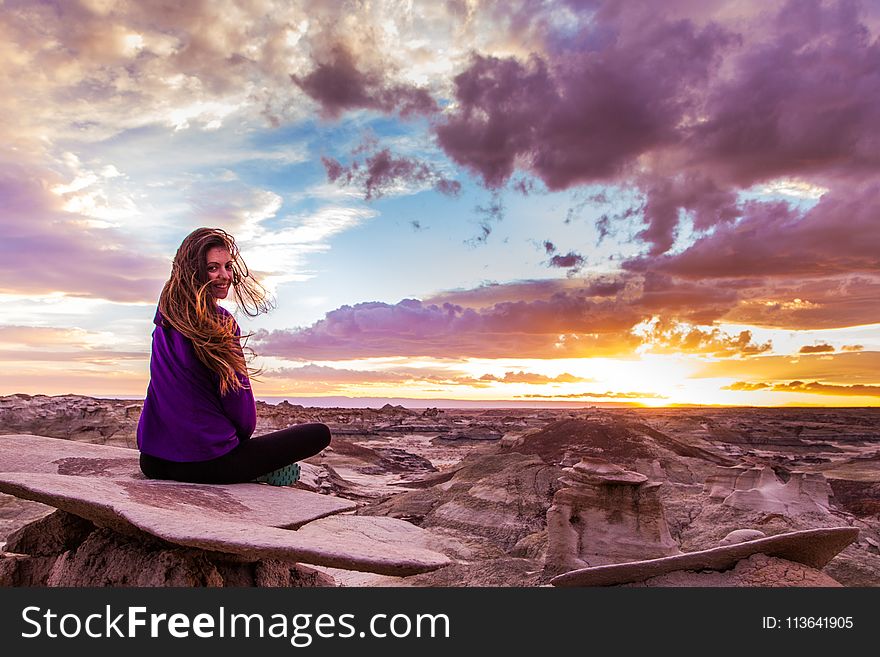 Woman Sits on Mountain Under Cloudy Sky at Sunset