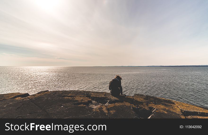 Person Sitting on Stone in Front of Sea Water