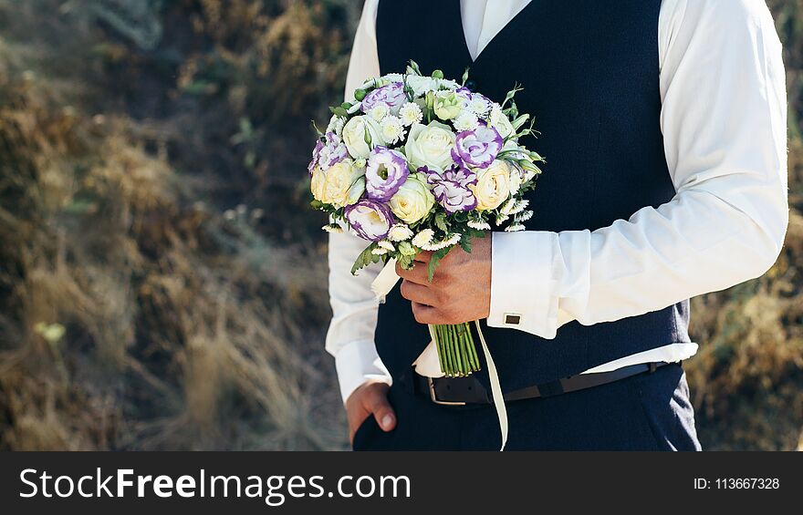 Wedding. The groom in a white shirt and waistcoat are holding bouquets of of white roses, hypericum, lisianthus, chrysanthemum, eustoma