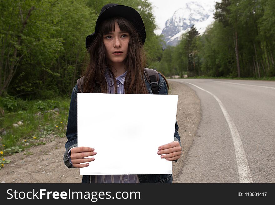 Your text here.Travel and hitch-hiking concept. Studio portrait of happy pretty young woman standing with empty blank.