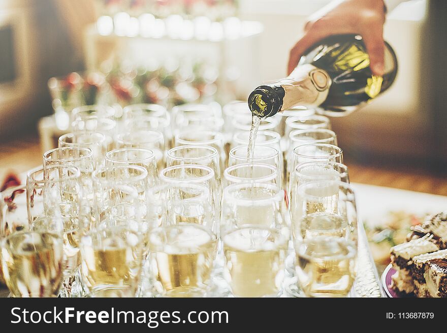 Waiter pouring champagne in stylish glasses at luxury wedding reception. rich celebration. expensive catering and service at feast. new year and christmas celebrations and drinks