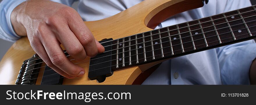 Male arms holding and playing classic shape wooden electric guitar closeup. Six stringed learning musical school education art leisure electrical vintage stage shop having fun enjoying hobby concept. Male arms holding and playing classic shape wooden electric guitar closeup. Six stringed learning musical school education art leisure electrical vintage stage shop having fun enjoying hobby concept