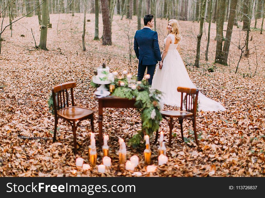 Beautiful wedding couple posing near the vintage table in the autumn forest. Beautiful wedding couple posing near the vintage table in the autumn forest.