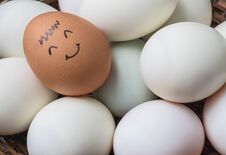 Closeup Brown Chicken Egg With Paint In Smile Face On Pile Of White Duck Egg On Wood Basket Background Stock Image