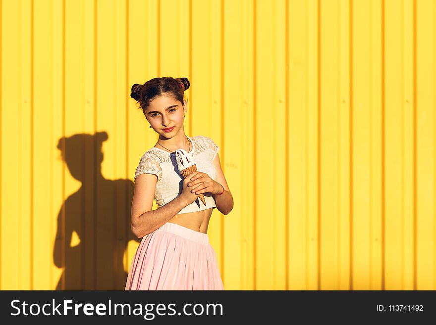 Portrait of a smiling girl with ice cream in hands on a yellow background.