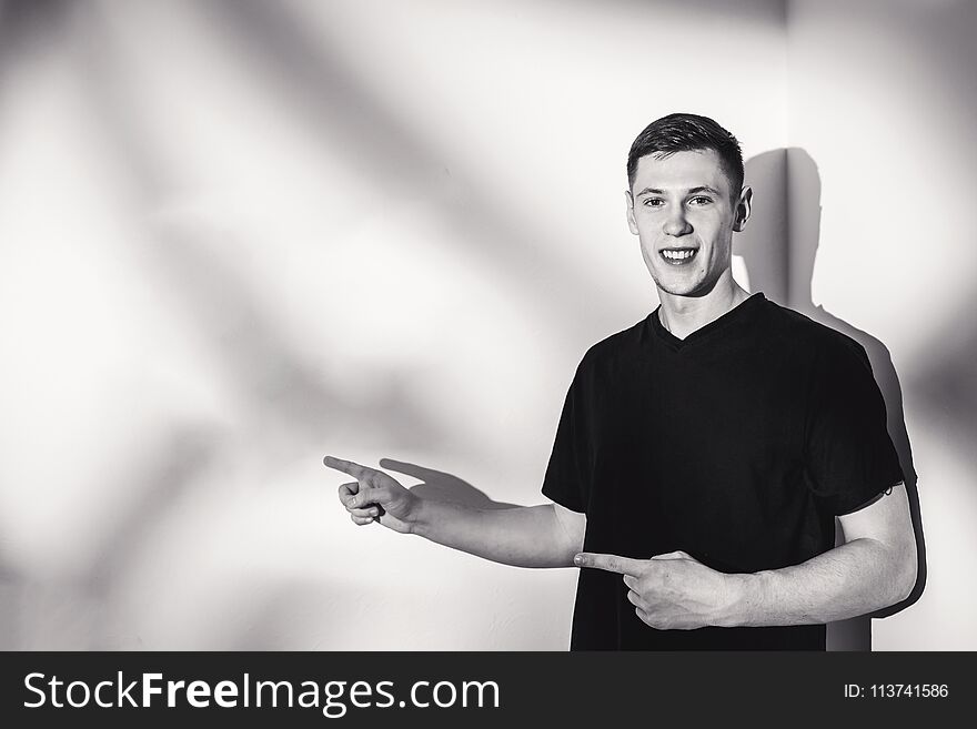 Portrait of handsome young man in black t-shirt poses over wall with contrast shadows. Copy space.