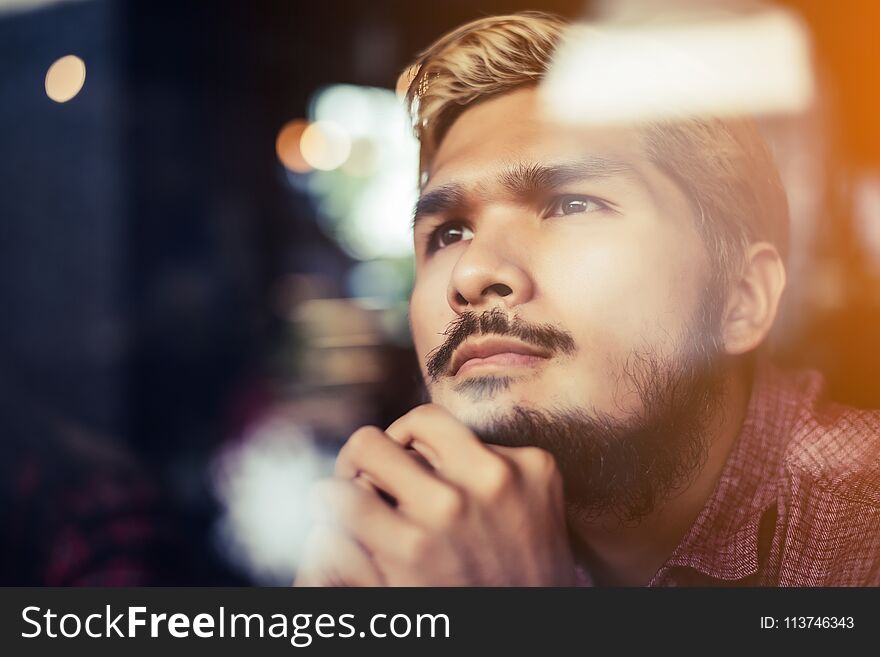 Pensive young hipster man sitting in coffee shop thinking and looking away.