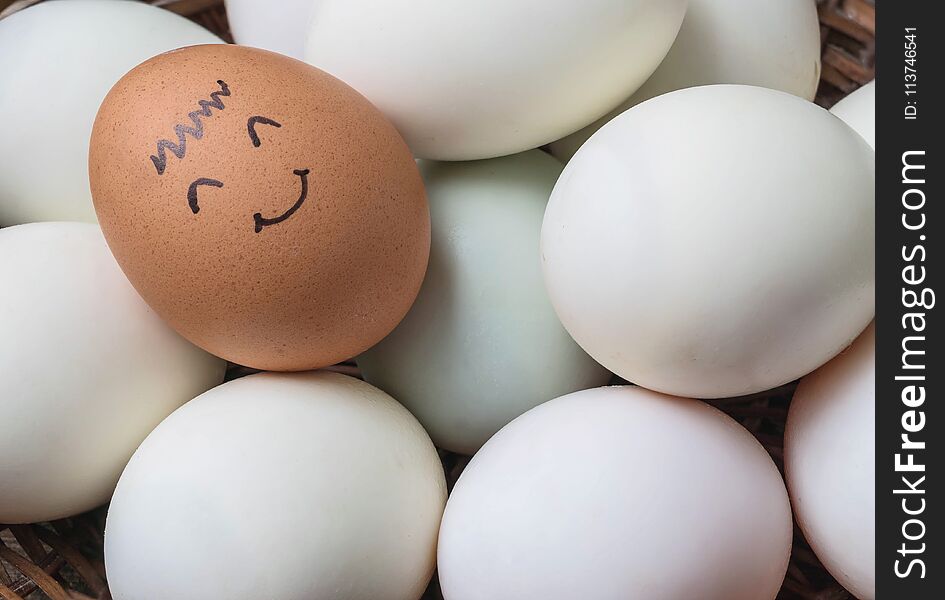 Closeup Brown Chicken Egg With Paint In Smile Face On Pile Of White Duck Egg On Wood Basket Background