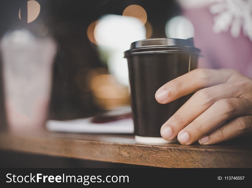 Close-up of young man holding coffee to take away at early morning at cafe.