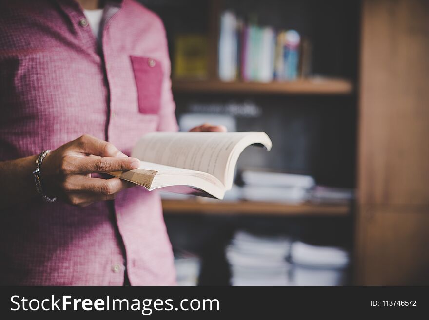 Young hipster man reading book in library background. Young hipster man reading book in library background