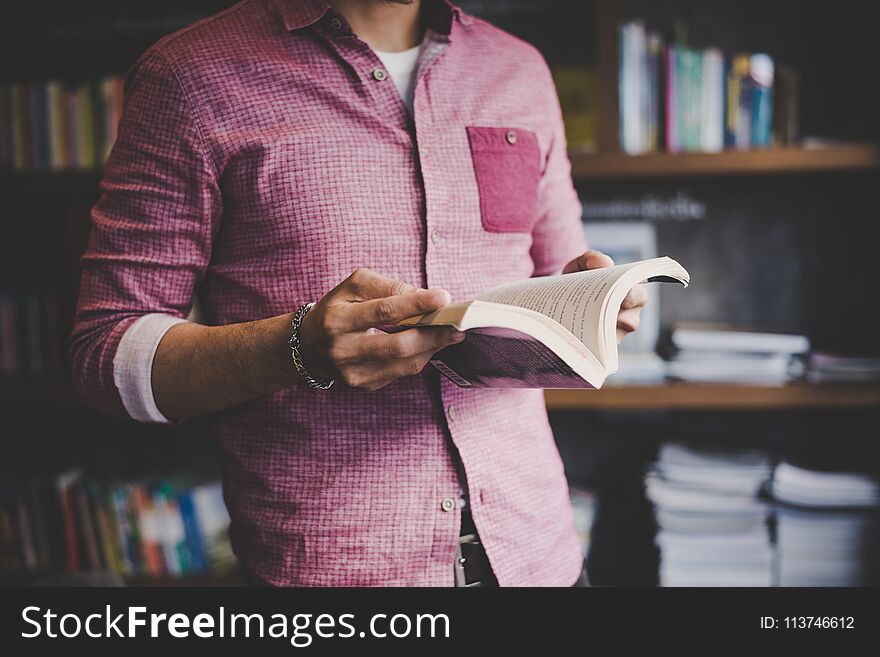 Young hipster man reading book in library.