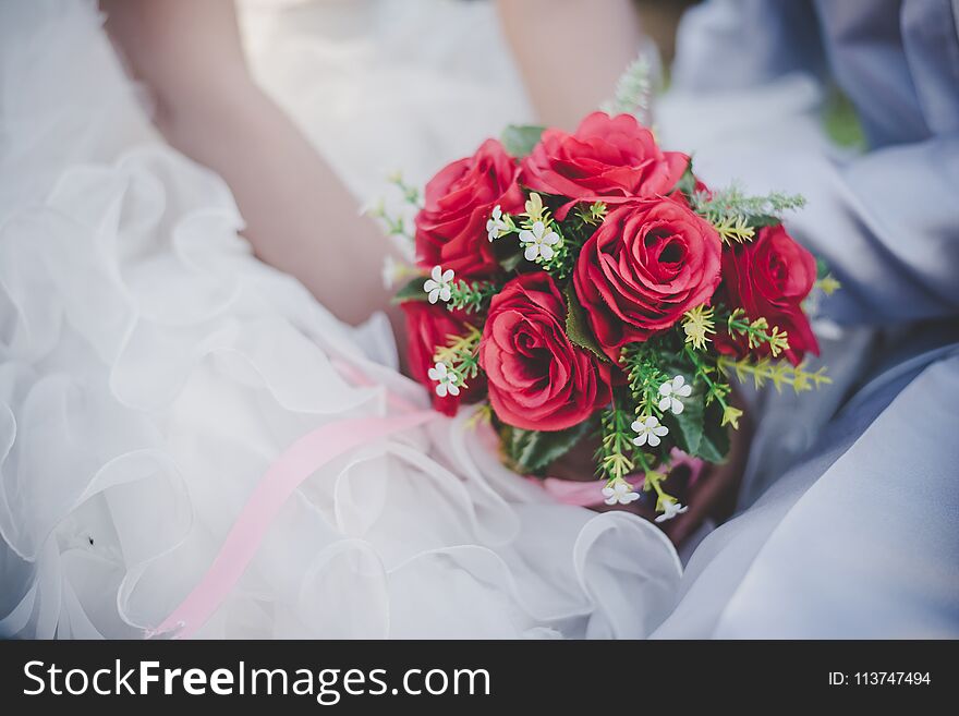 Bride holds a wedding red rose bouquet in hands, the groom hugs his bride together. Wedding lover concept.