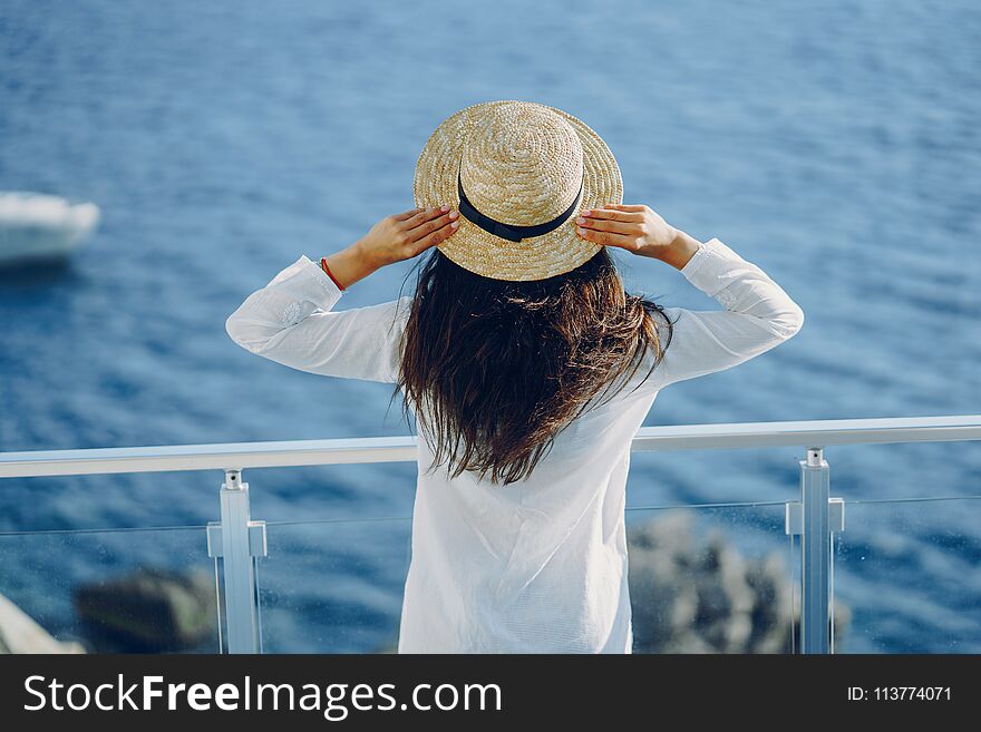 A beautiful young girl in a straw hat standing on a summer terrace and looking at the ocean. A beautiful young girl in a straw hat standing on a summer terrace and looking at the ocean