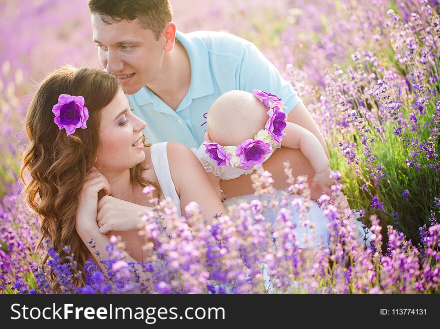 Mom, Dad and their little daughter in a beautiful wreath are walking in a lavender field. Life in Provence. Brunette in white dress with her family. Mom, Dad and their little daughter in a beautiful wreath are walking in a lavender field. Life in Provence. Brunette in white dress with her family
