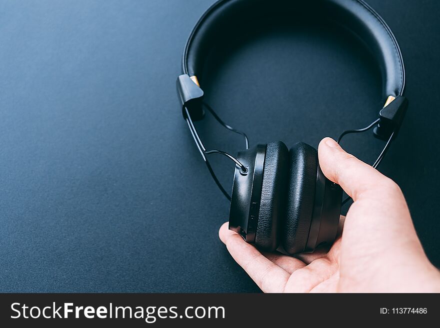 Wireless headphone is hold or hanging by a man right hand with black background and copy space for text. Wireless headphone is hold or hanging by a man right hand with black background and copy space for text