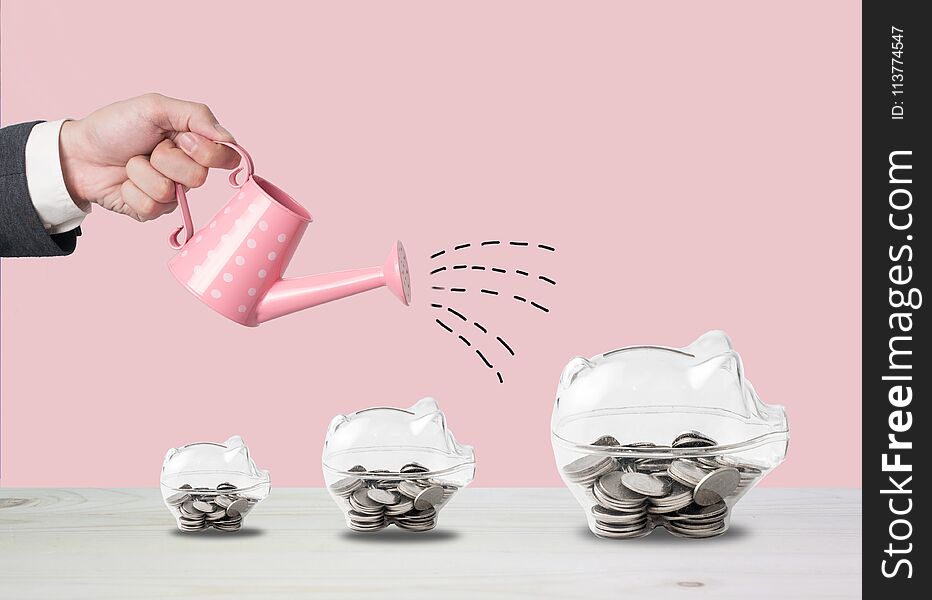 Transparent piggy bank filled with coins on wood background.Saving investment colorful concept.Watering can and money growth drawn concept for business investment, savings and making money.