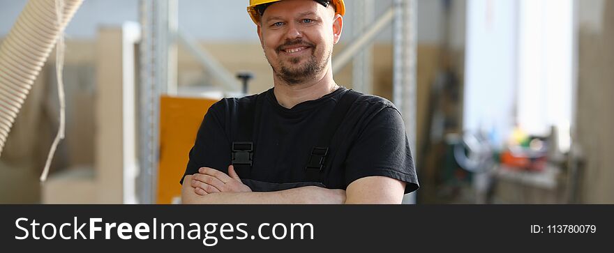 Portrait of young attractive man in work clothes and yellow helmet crossed arms smiling at shop for manufacturing furniture and details home interior