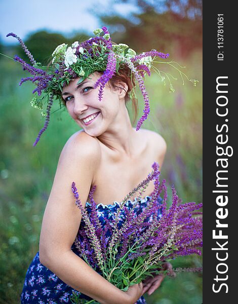 Young laughing woman in a wreath with violet flowers in her hands