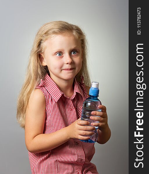 Adorable little girl with long hair holding a bottle of water on gray background