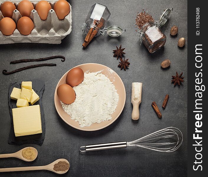 Flour and eggs in bowl, foods and spices on desktop, on grey background