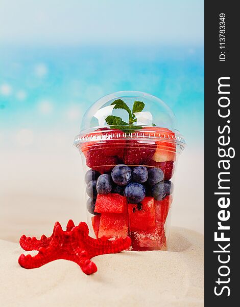 Plastic cup full of fresh cut fruits and berries on the sea coast. Paradise vacations concept. Copy space