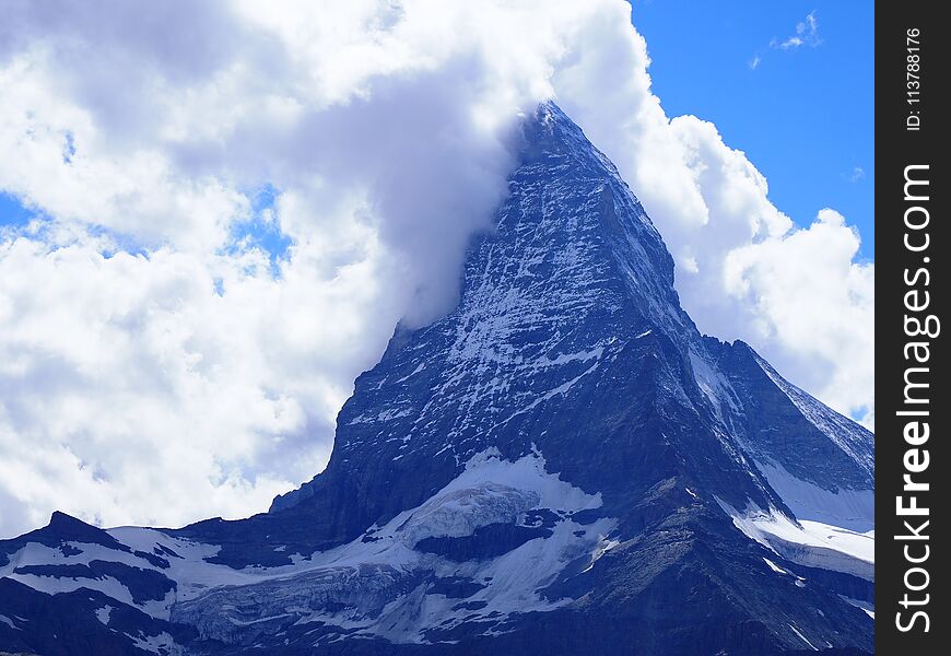 Scenic view of Matterhorn mount in clouds and alpine mountains range landscapes in swiss Alps seen from Gornergrat in SWITZERLAND with cloudy blue sky in 2017 warm sunny summer day, Europe on July. Scenic view of Matterhorn mount in clouds and alpine mountains range landscapes in swiss Alps seen from Gornergrat in SWITZERLAND with cloudy blue sky in 2017 warm sunny summer day, Europe on July.