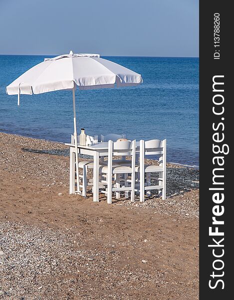 White wooden table with four chair and umbrella on beach with blue sea