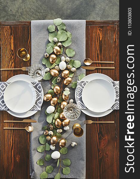 Top view of easter golden eggs, plates and glasses on table in restaurant