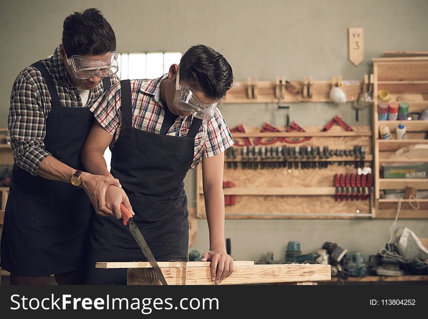 Father teaching his son how to saw wooden board. Father teaching his son how to saw wooden board
