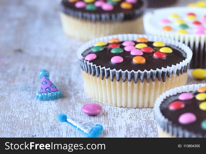 Cupcakes with sugar coated chocolate on a white wooden background