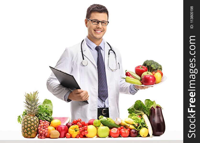 Doctor holding a clipboard and a plate behind a table with t and vegetables isolated on white background. Doctor holding a clipboard and a plate behind a table with t and vegetables isolated on white background