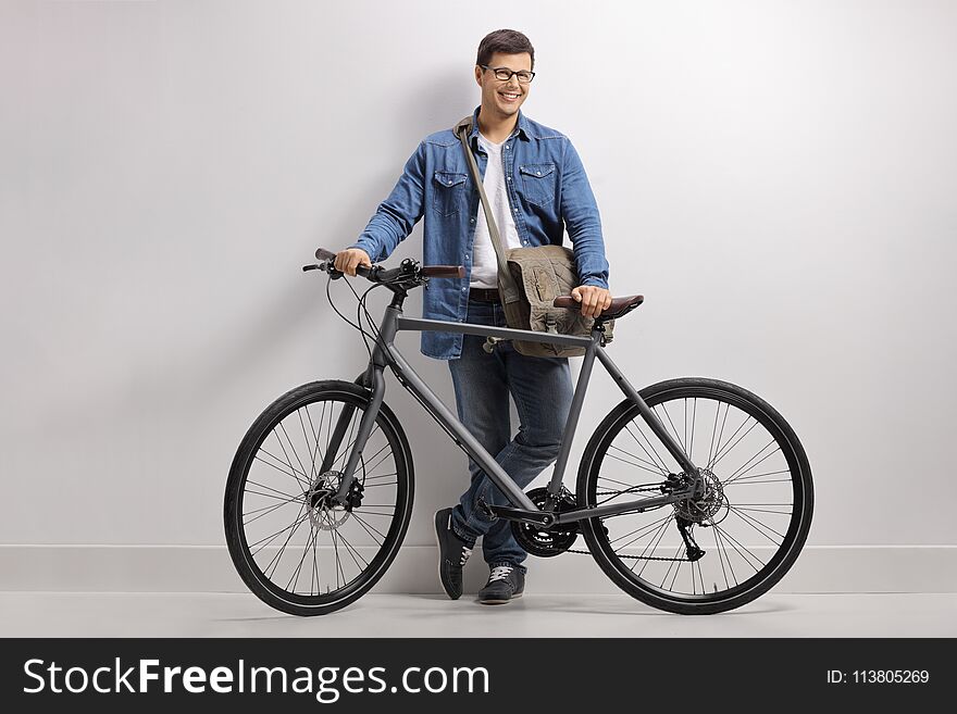 Full length portrait of a young man with a bicycle leaning against a wall and smiling