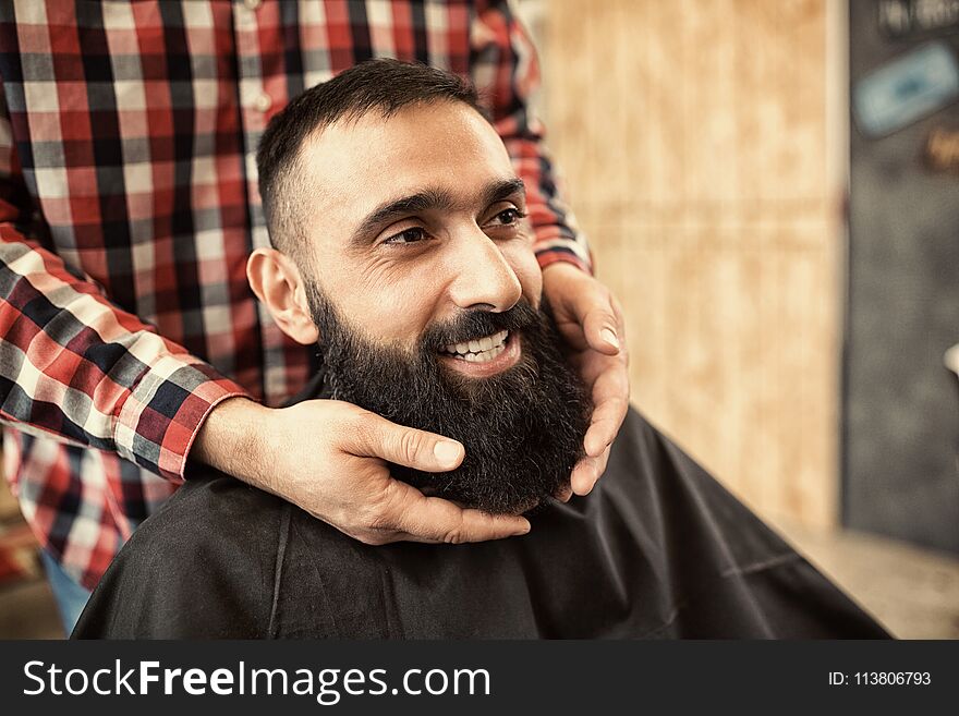 Smiling satisfied hipster client visiting barber shop, looking g